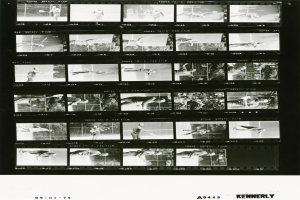 Schwarzes und weißes Foto eines konzentrierten Mannes in einem weißen Hemd und Shorts, der Tennis spielt und einen Schläger in seiner rechten Hand hält, mit einem Filmstreifen im Hintergrund.