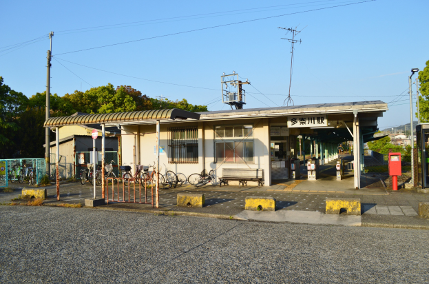 Ein Bahnhof mit Fahrrädern davor, eine Straße unten und Häusern, Bäumen, Pfählen, Drähten und einem klaren blauen Himmel im Hintergrund.