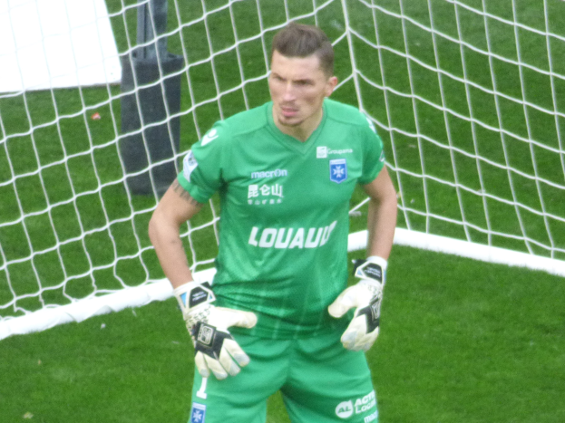 Ein Torwart in grüner Uniform steht vor einem Fußballtor auf saftig grünem Rasen, trägt Handschuhe.