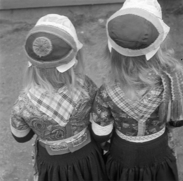 Zwei junge Mädchen in traditionellen bayerischen Kleidern und Hüten stehen nebeneinander vor einer Wand in einem Schwarz-Weiß-Foto.